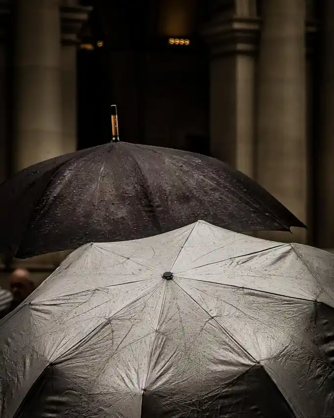 Two black umbrellas opened side by side in a stone colonnade
